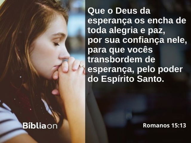 Uma mulher dentro de uma igreja, vista de lado, ajoelhada e com as mãos juntas, de olhos fechados em oração. Texto da imagem é da carta aos Romanos, capítulo quinze, verso treze, que diz: Que o Deus da esperança os encha de toda alegria e paz, por sua confiança nele, para que vocês transbordem de esperança, pelo poder do Espírito Santo.